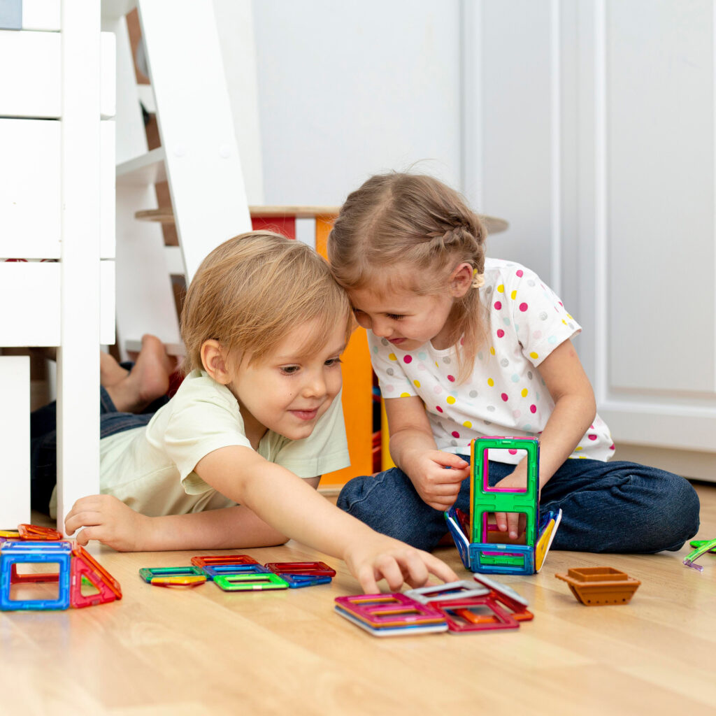 Zwei Kinder spielen im Zimmer mit Magnetbausteinen